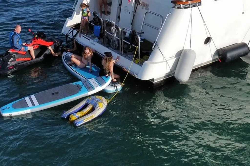 A rider on a jet ski beside a yacht swim platform with paddleboards in the water